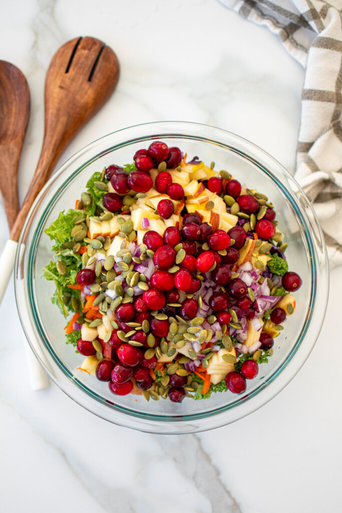 simple cranberry kale salad with homemade dressing in a glass mixing bowl on a white marble countertop.