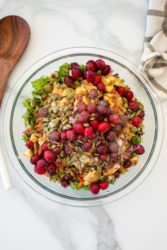simple cranberry kale salad with homemade dressing in a glass mixing bowl on a white marble countertop.