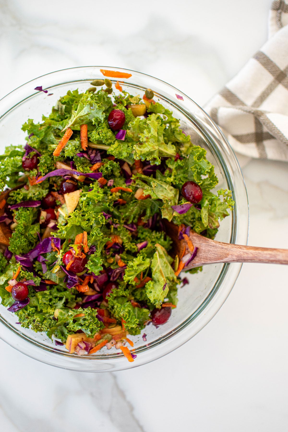 simple cranberry kale salad with homemade dressing in a glass mixing bowl on a white marble countertop.