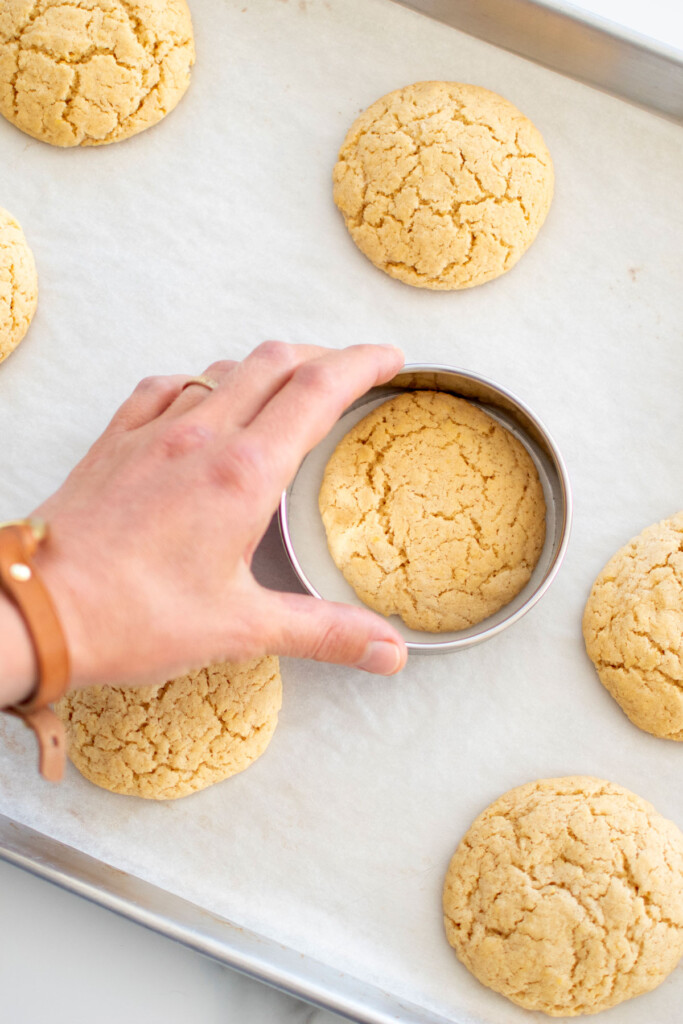 woman swirling cookies with a cookie cutter to round them out on a baking sheet.