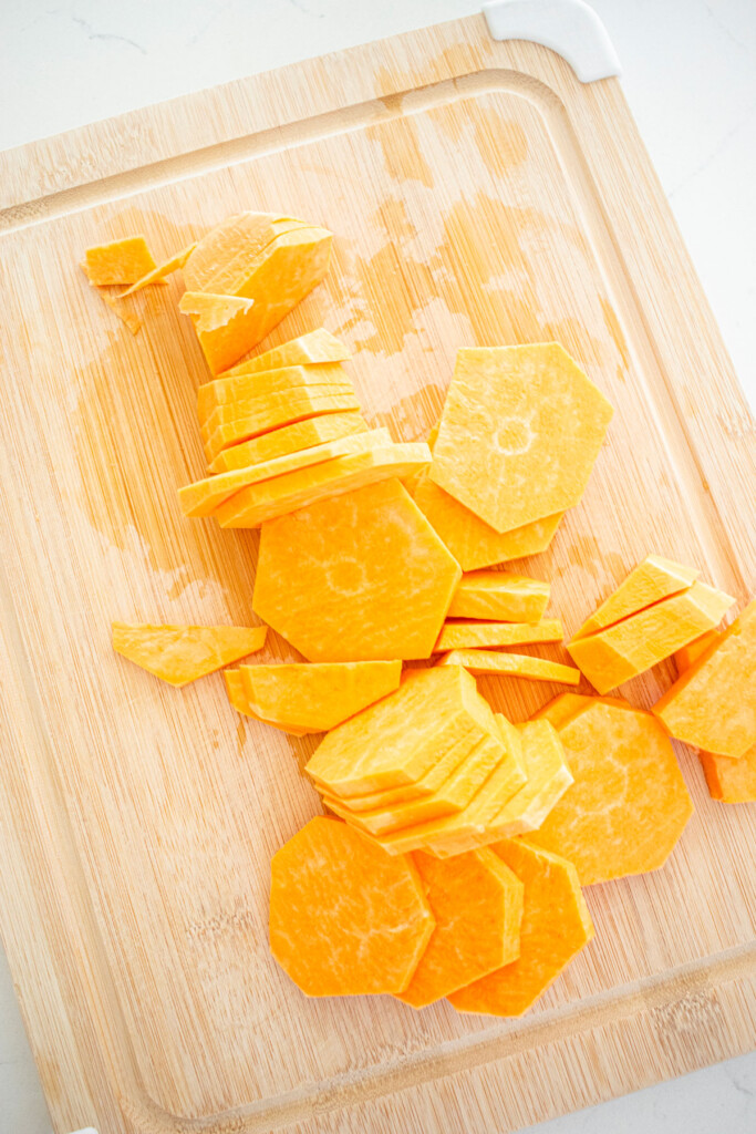 sweet potatoes peeled and sliced on a wood cutting board on a white kitchen counter.