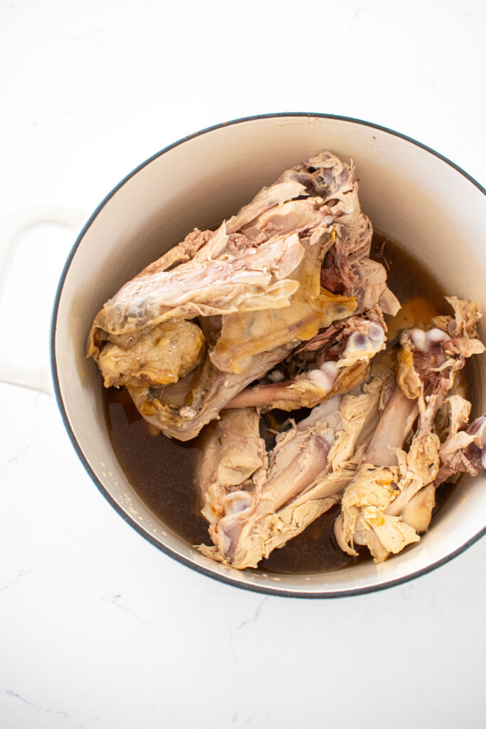 turkey carcass in a white dutch oven on a marble counter.