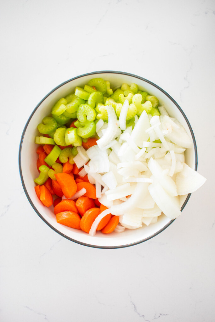 bowl of chopped carrots, celery and onion on a white marble counter.