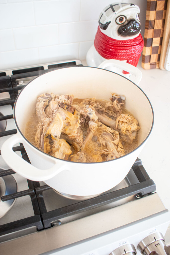 turkey carcass simmering in bone broth in a dutch oven on a stovetop.