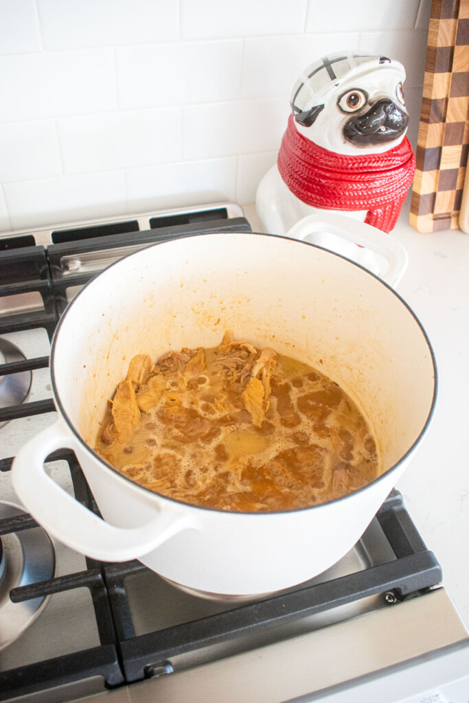 turkey meat removed from bones simmering in bone broth in a dutch oven on the stoveop.
