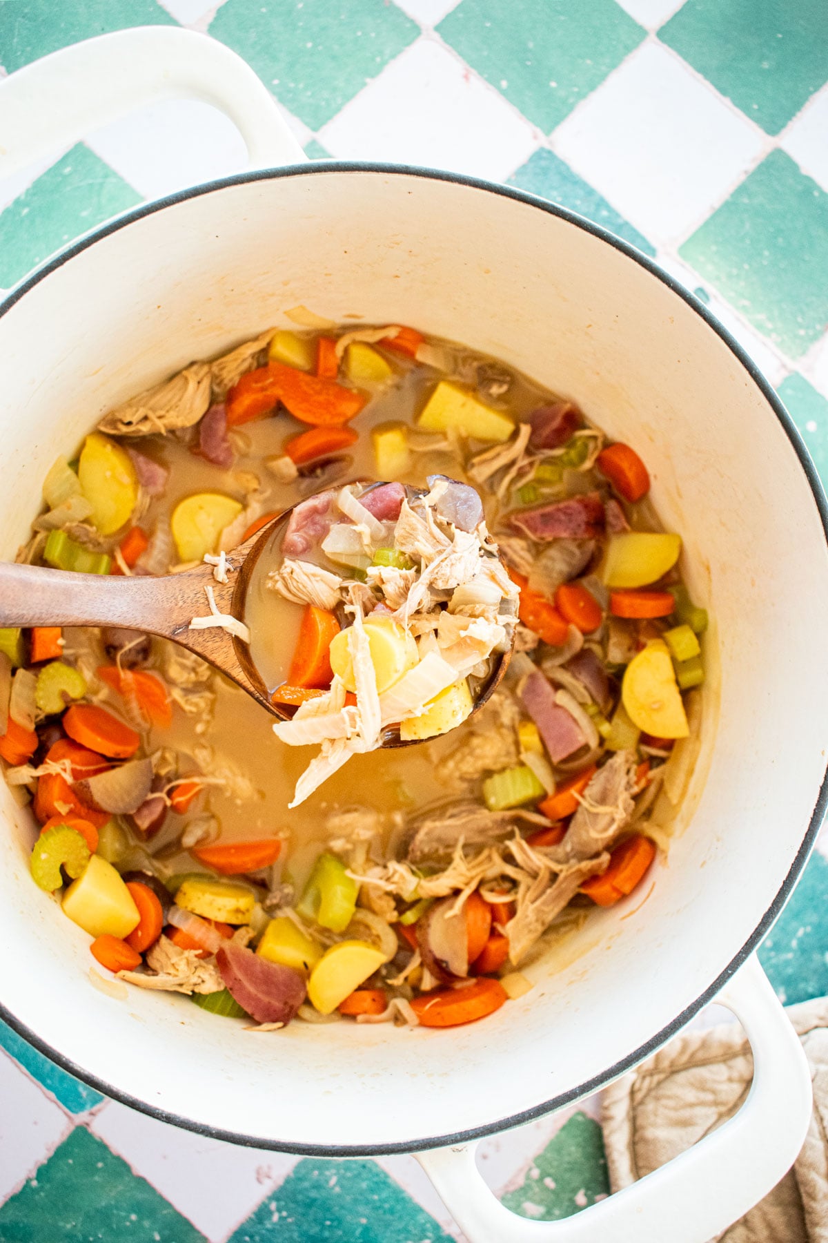 turkey carcass soup with bone broth in a bowl with a side plate of bread and butter on a green tile table.