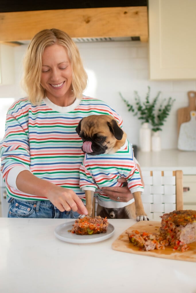 woman feeding a pug turkey meatloaf for dogs at the kitchen counter.