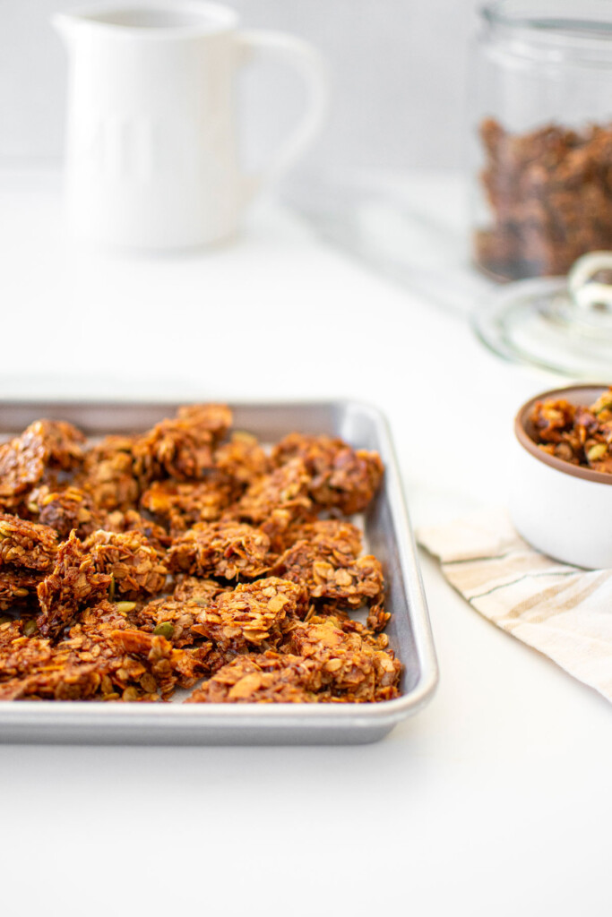 baking sheet of maple cinnamon olive oil granola on a white marble counter with a milk pitcher in the background.