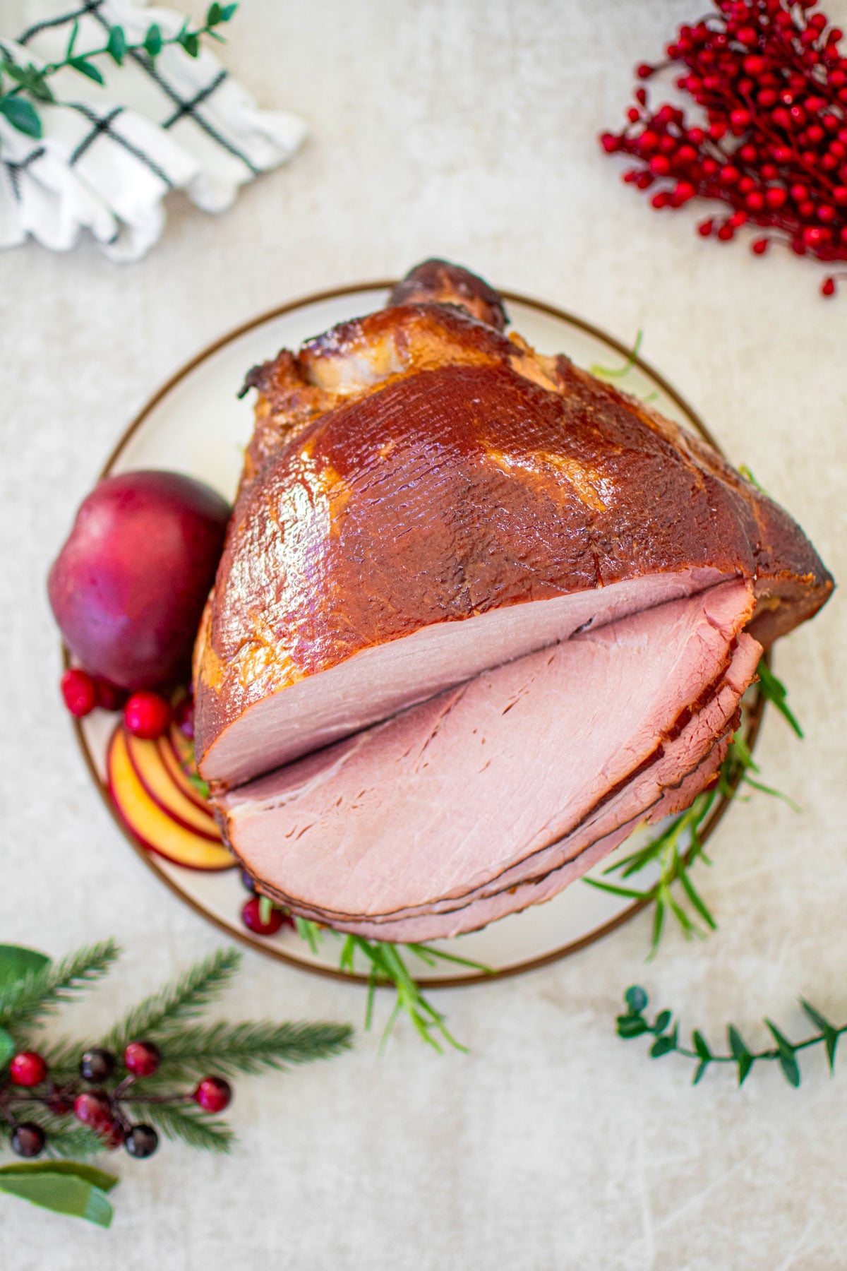 apple cider honey baked ham cut into slices on a plate garnished with apple, cranberries and fresh rosemary.
