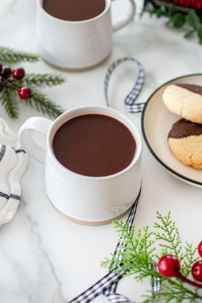 bone broth hot cocoa in a white mug on a marble countertop with christmas cookies.