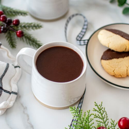 bone broth hot cocoa in a white mug on a marble countertop with christmas cookies.