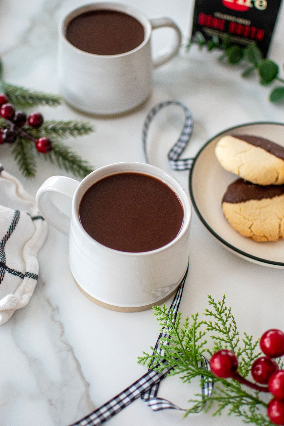 bone broth hot cocoa in a white mug on a marble countertop with christmas cookies.