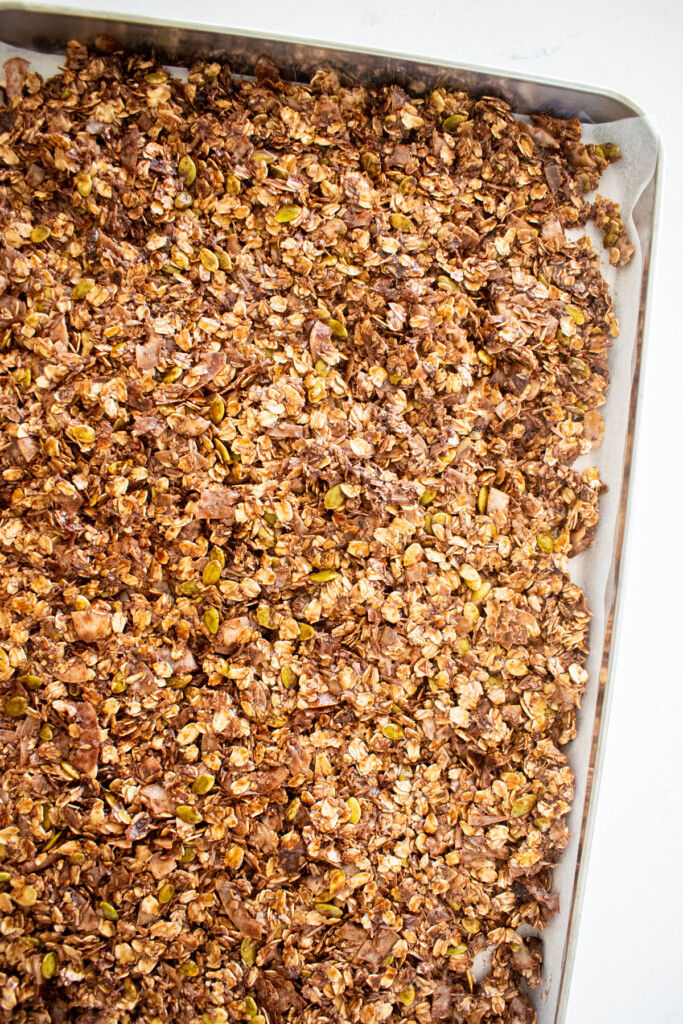 chocolate peppermint olive oil granola spread out onto a baking sheet on a marble counter.
