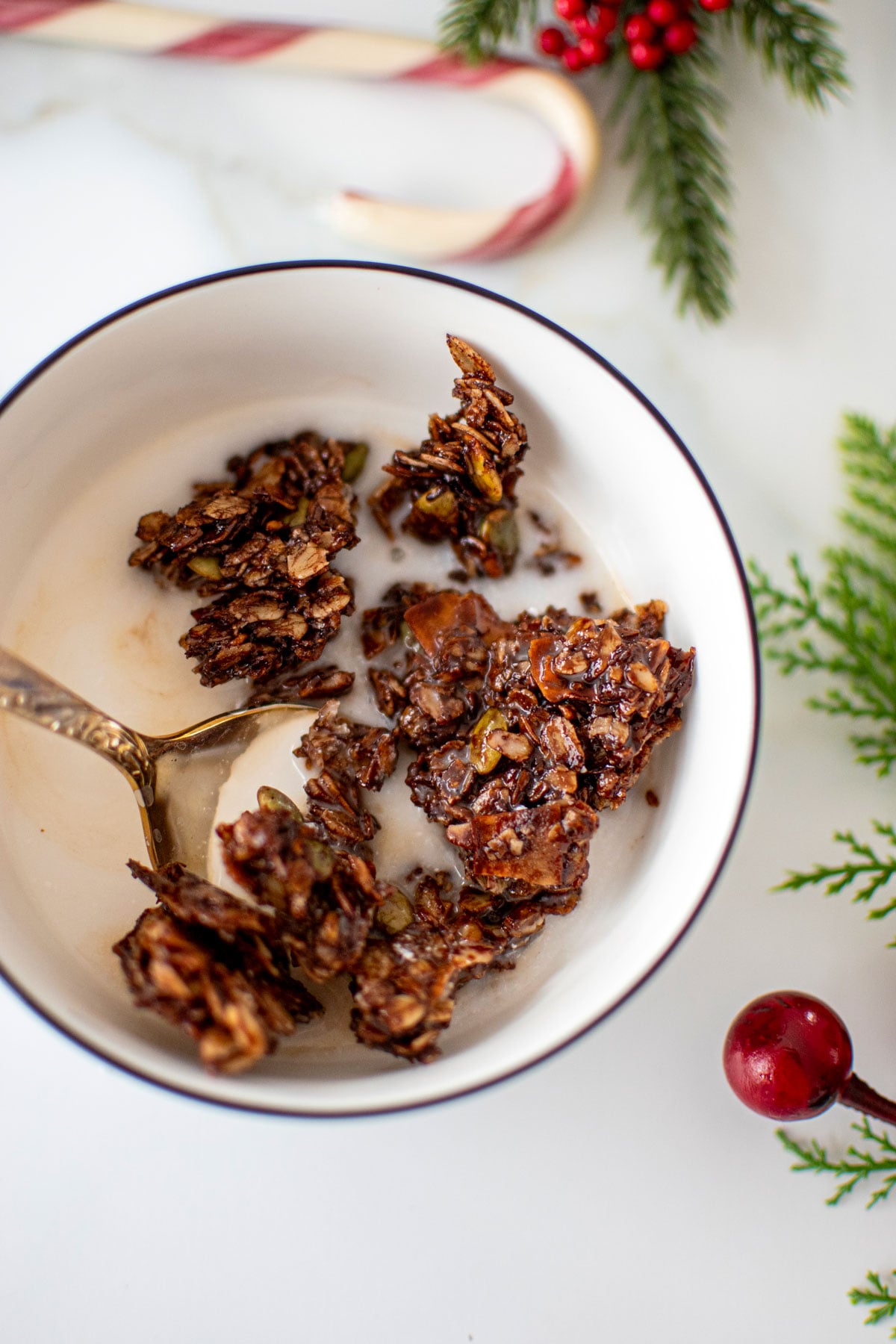 bowl of chocolate peppermint olive oil granola with milk and a spoon on a marble counter.