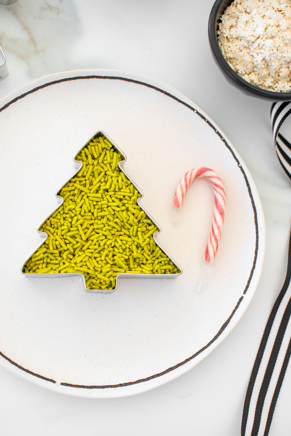 tree cookie cutter with green sprinkles in it on a white plate.