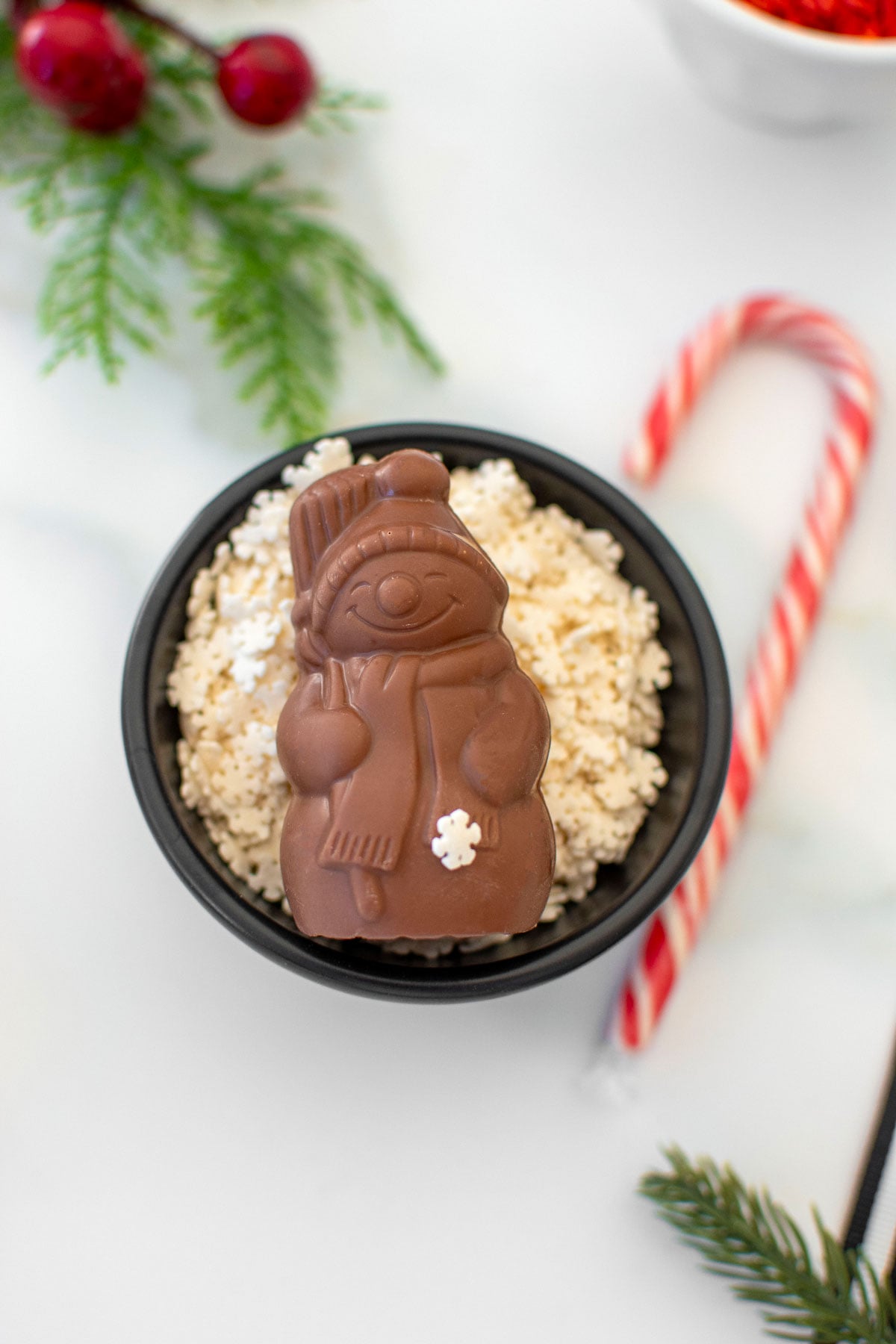 organic chocolate santa in a bowl of snowflake sprinkles on a white marble counter.