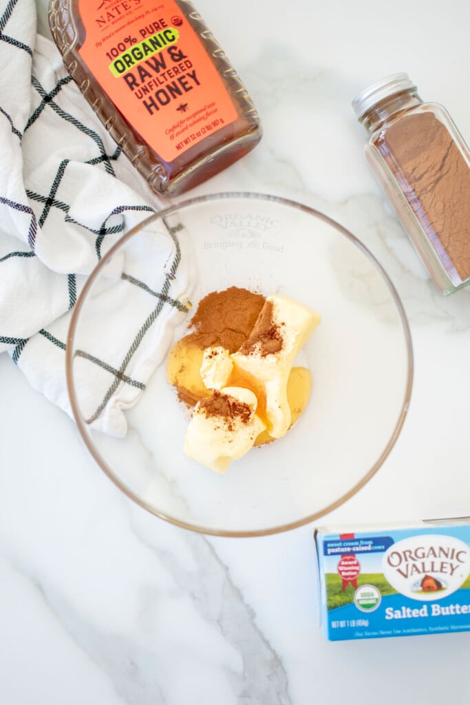 butter, honey, and cinnamon in a mixing bowl on a white countertop.