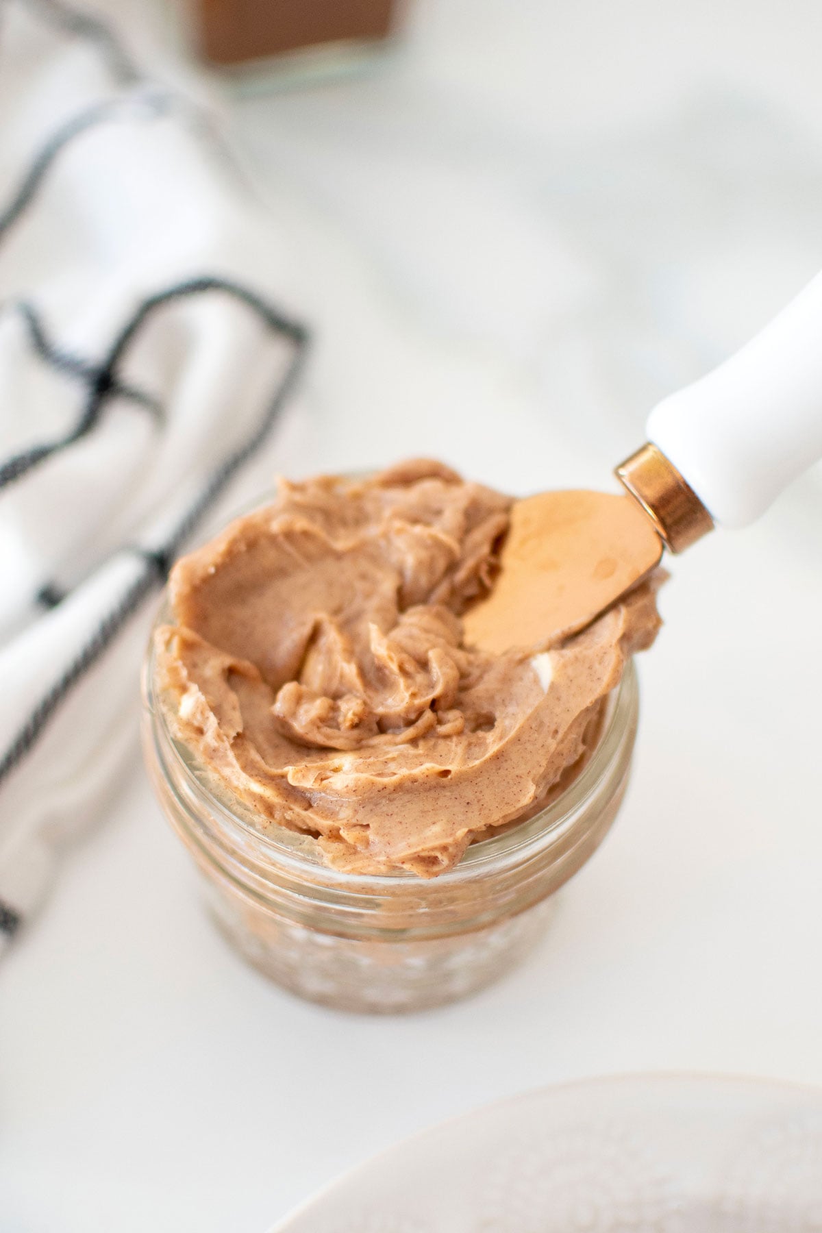 cinnamon honey butter spread in a small glass jar with a knife on a white countertop.