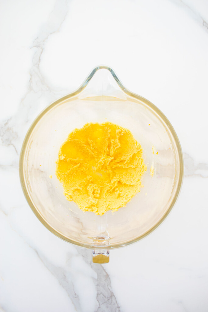 creamed butter sugar and orange zest in a glass mixing bowl on a marble counter.