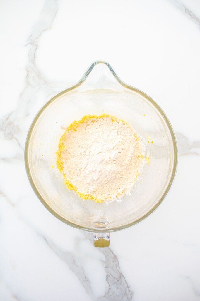 ingredients for cranberry orange biscotti with sourdough discard in a glass mixing bowl on a marble counter.