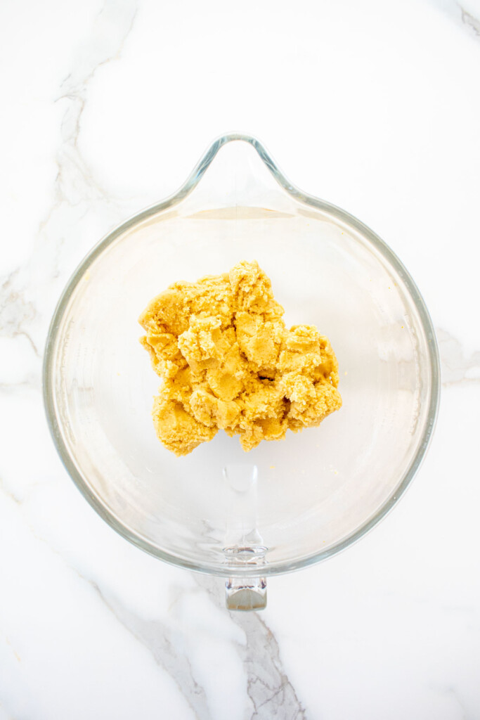 orange biscotti cookie dough in a glass mixing bowl on a marble counter.