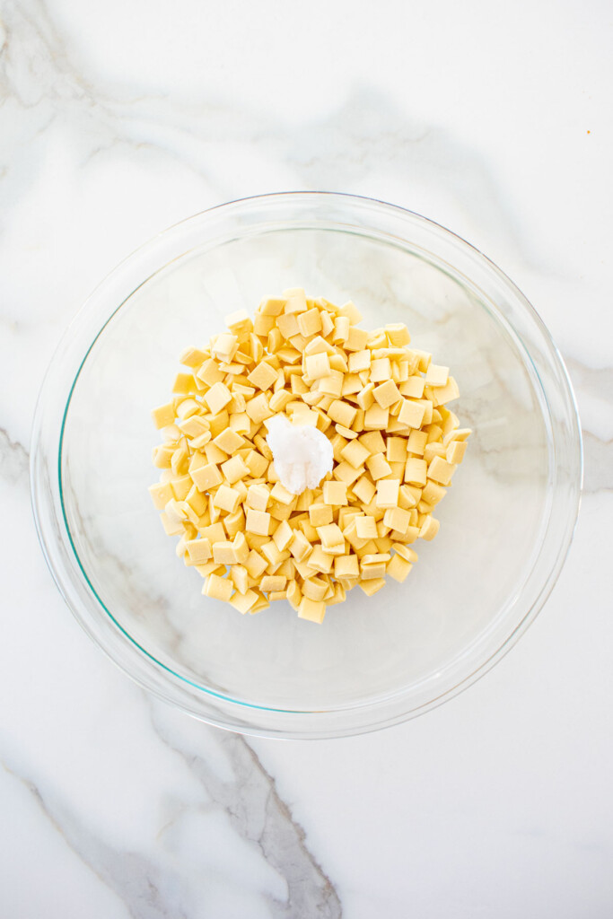 white chocolate chunks with coconut oil in a glass mixing bowl on a white marble counter.