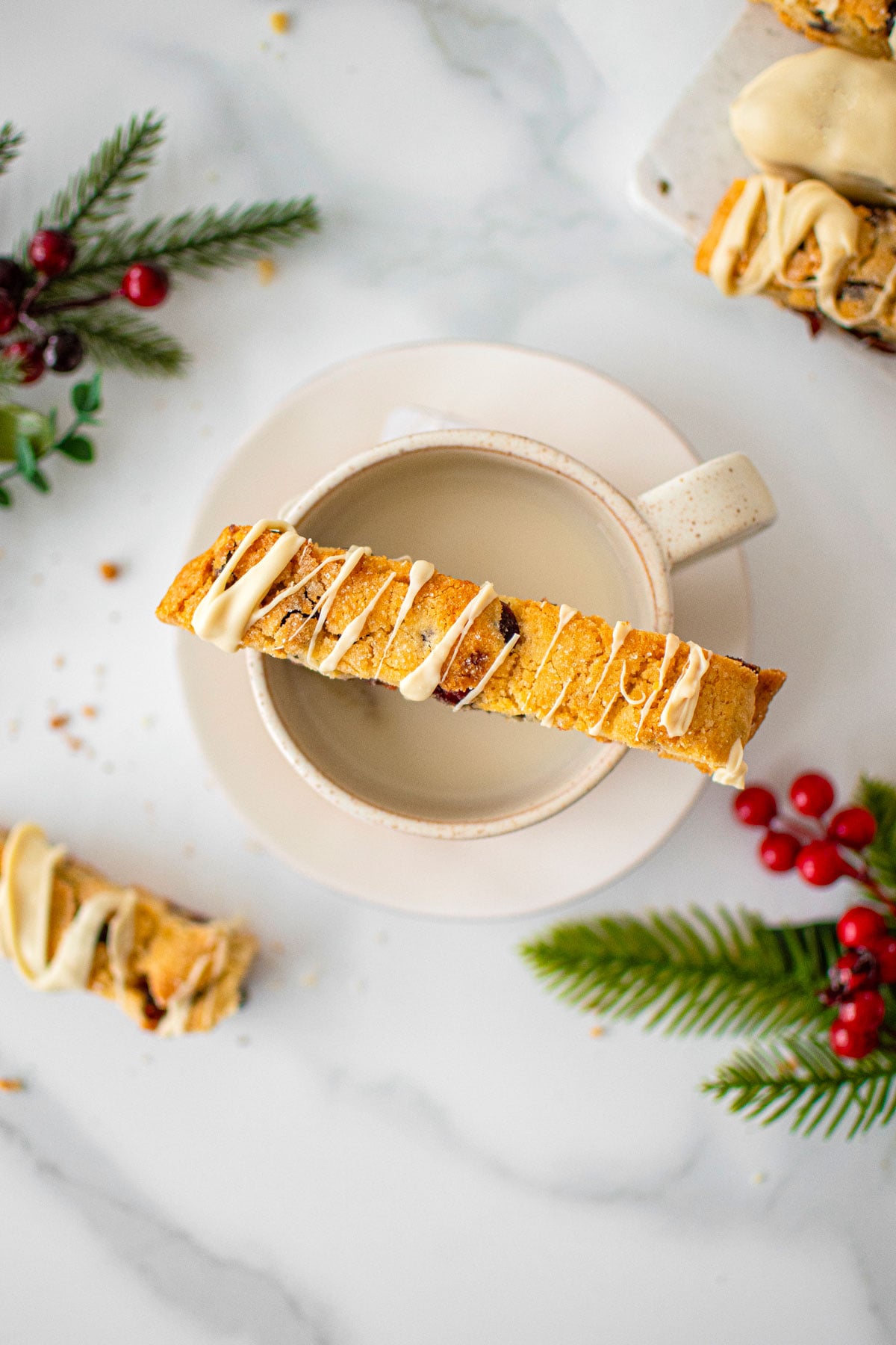 cranberry orange biscotti on top of a mug with tea on a white marble counter.