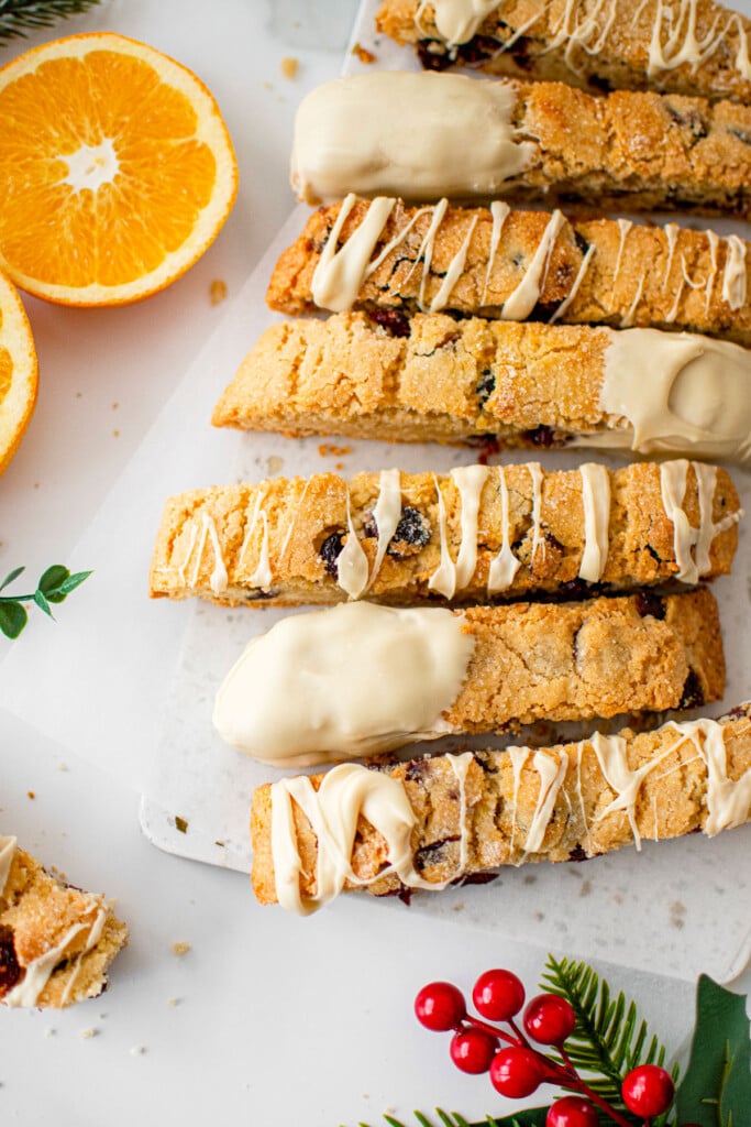 cranberry orange biscotti with sourdough discard pieces on a white marble board with fresh orange slices.