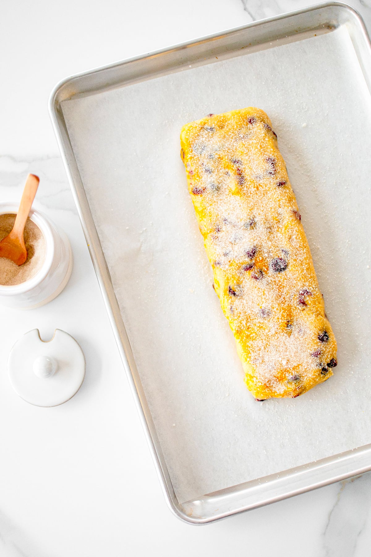 cranberry orange biscotti with sourdough discard cookie dough log on a baking sheet sprinkled with cane sugar.