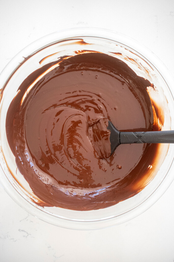 melted dark chocolate in a glass mixing bowl on a white marble counter.