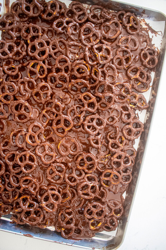 pretzel twists covered in chocolate on a baking sheet on a marble counter.