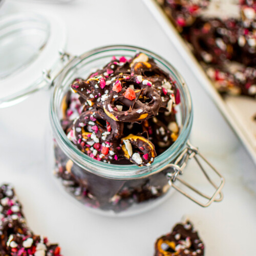 dark chocolate peppermint pretzel bark in a glass jar on a white marble counter.