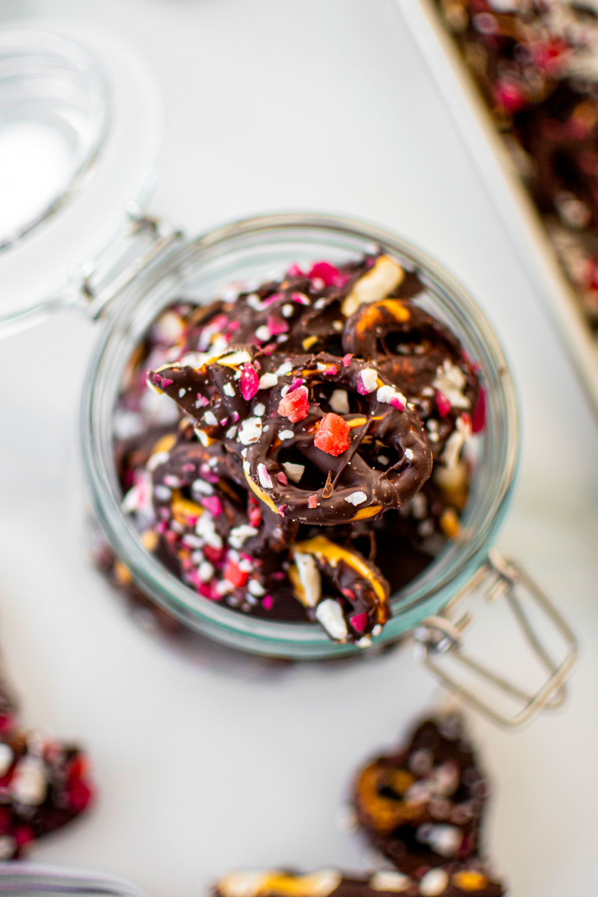 dark chocolate peppermint pretzel bark in a glass jar on a white marble counter.