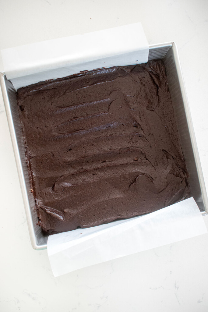 brownie batter spread into a baking pan on a white marble counter.