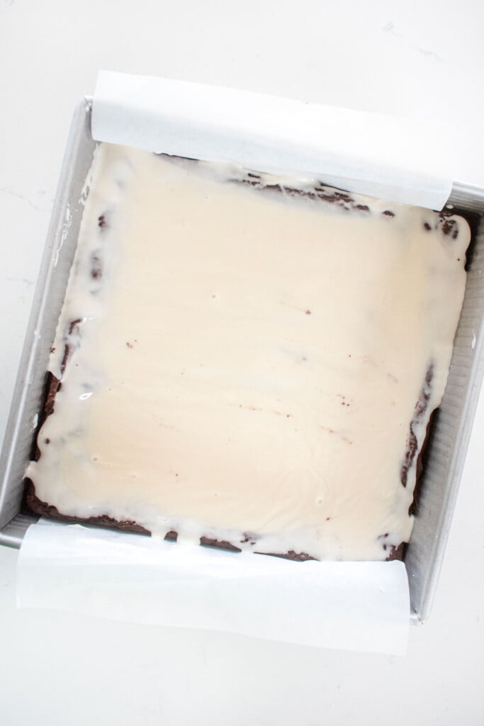 brownies in a baking pan with a white icing on top on a marble counter.