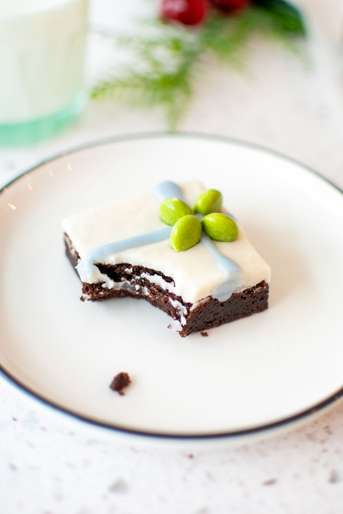 christmas present brownie on a white plate with a bite taken out on a marble counter with a glass of milk.
