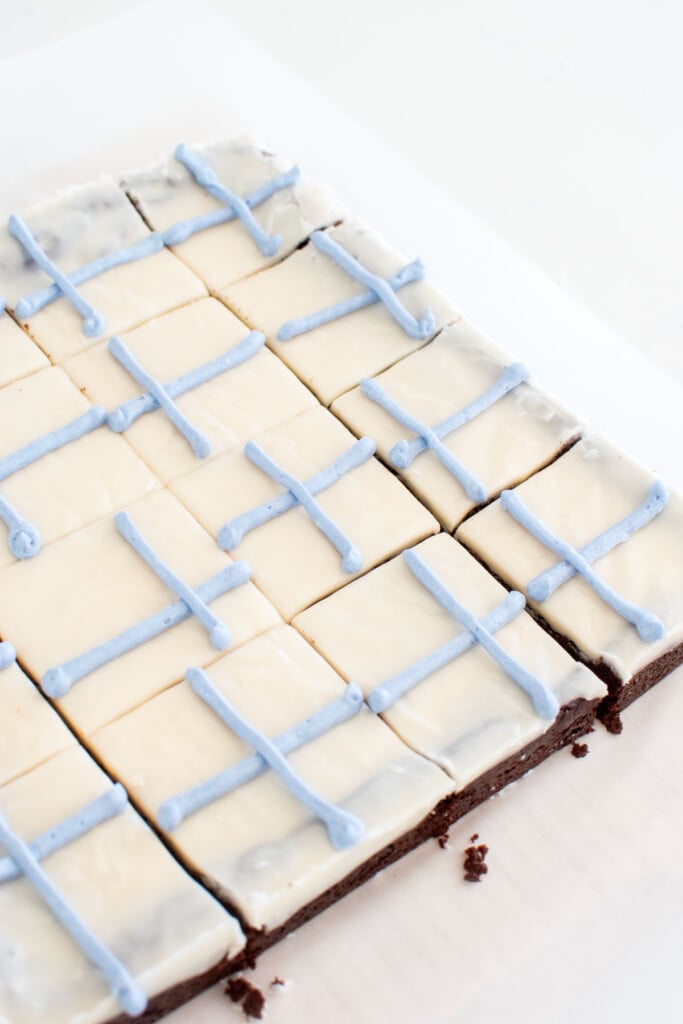 brownies cut into squares with blue "ribbon" piped onto them on a white marble counter.