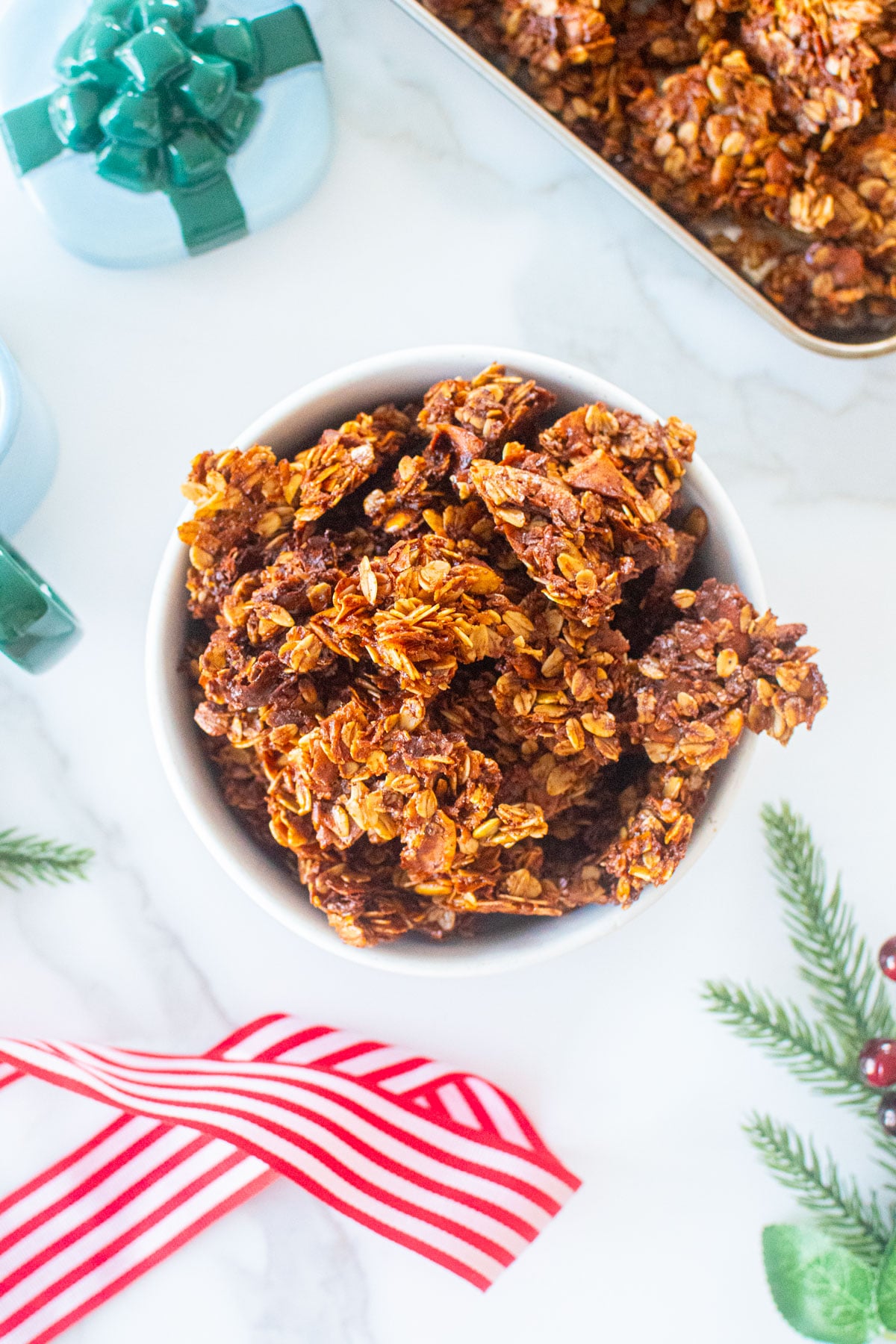 gingerbread granola clusters in a bowl on a white marble counter with holiday ribbon.