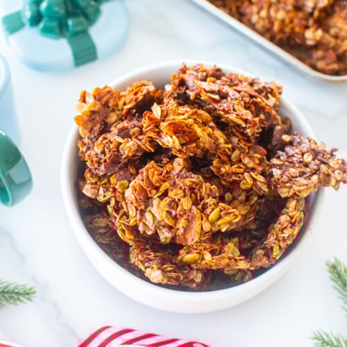 gingerbread granola clusters in a bowl on a white marble counter with holiday ribbon.