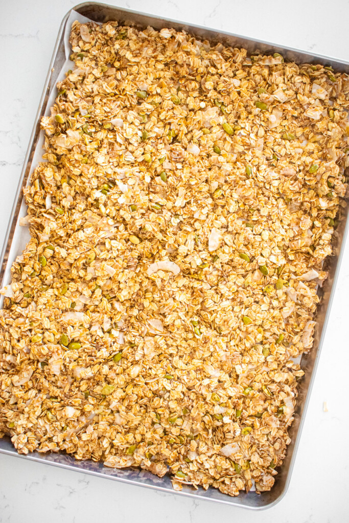 healthy gingerbread granola spread out onto a baking sheet ready to go into the oven.