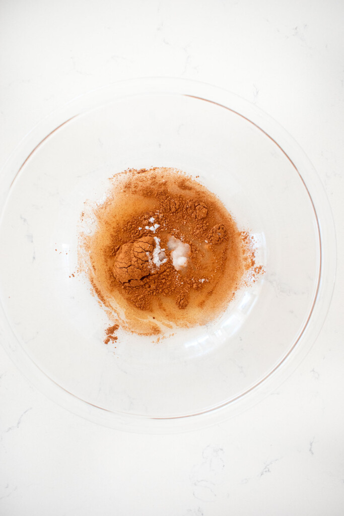 aquafaba in a glass mixing bowl with cinnamon and salt on a marble counter.