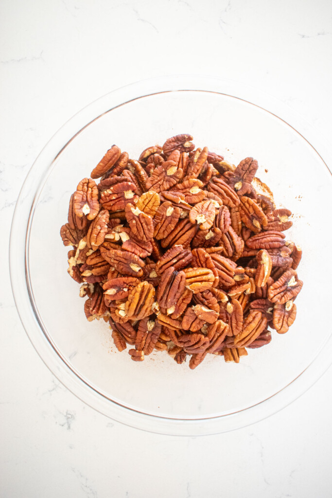 ingredients for candied pecans in a glass mixing bowl on a marble counter.