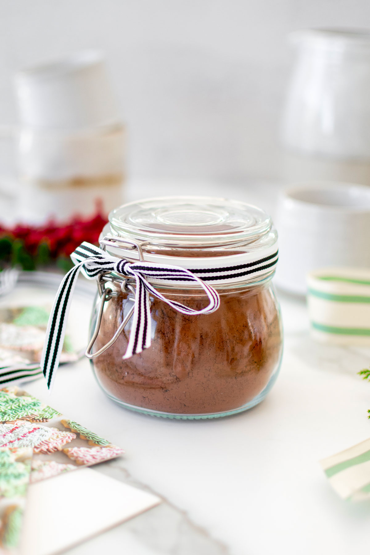glass jar of homemade hot cocoa mix for gifts tied with a ribbon on a white marble counter.