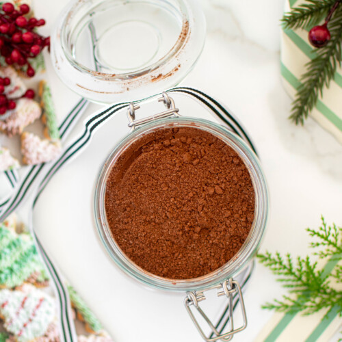 glass jar of homemade hot cocoa mix for gifts with a ribbon on a white marble counter.
