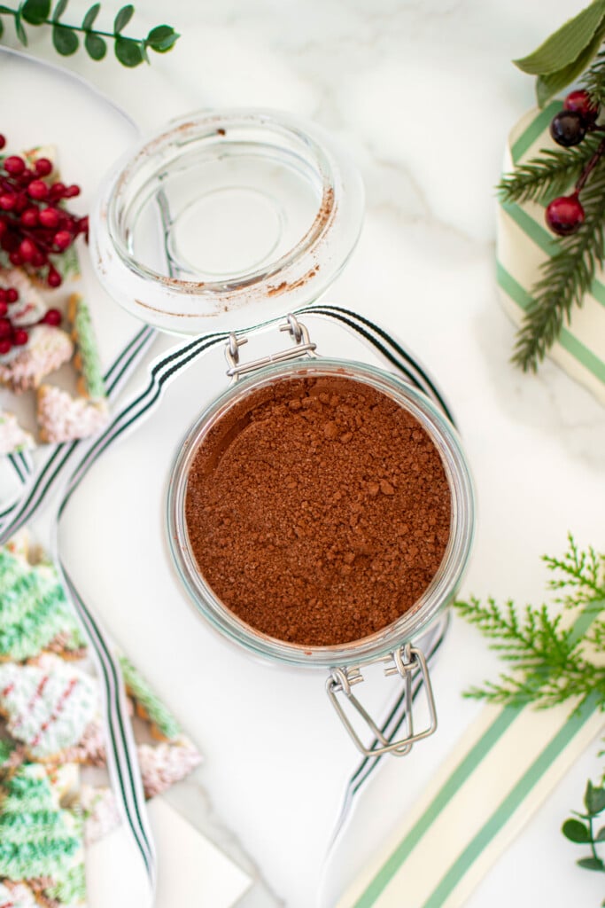 glass jar of homemade hot cocoa mix for gifts with a ribbon on a white marble counter.