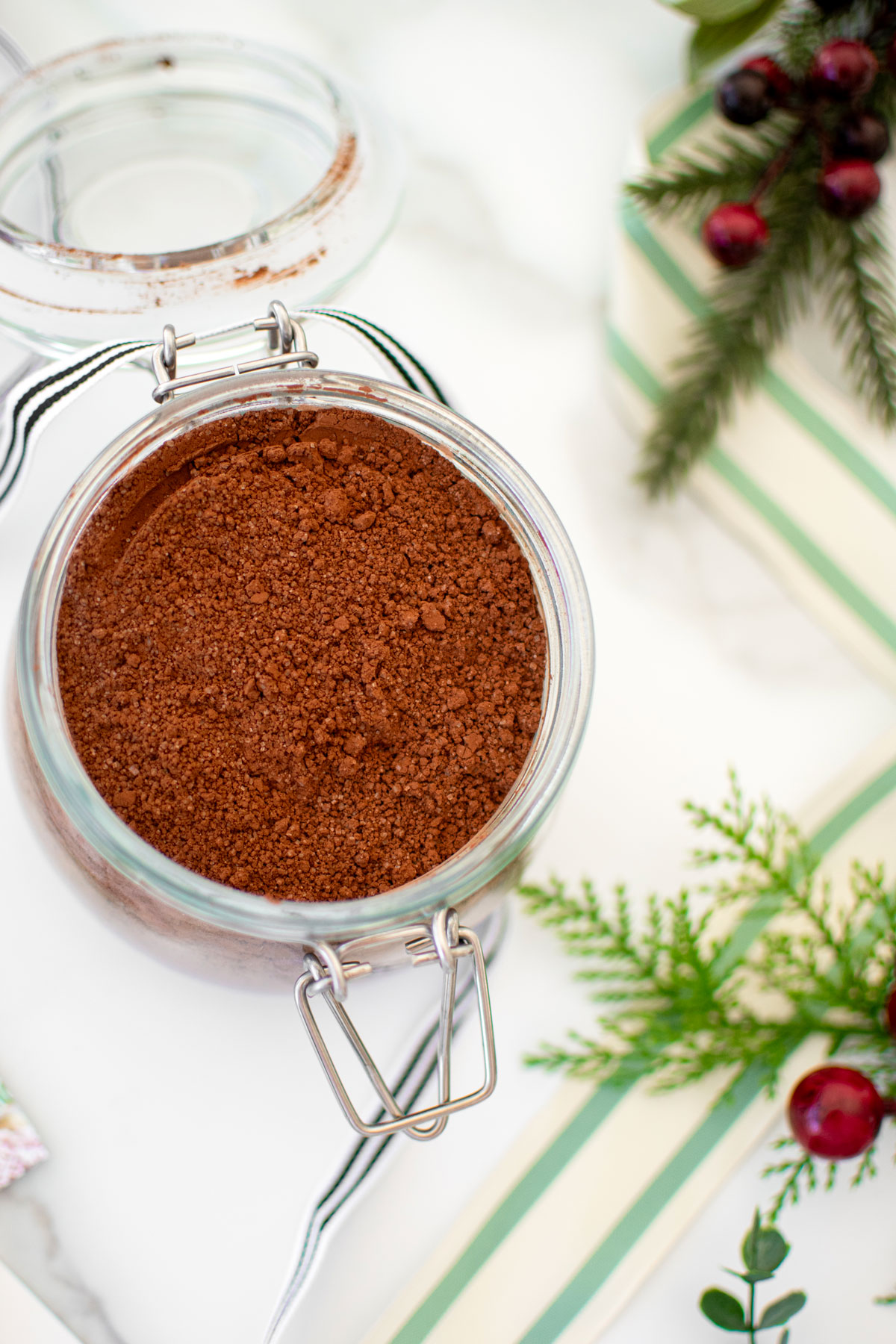 glass jar of homemade hot cocoa mix for gifts with a ribbon on a white marble counter.