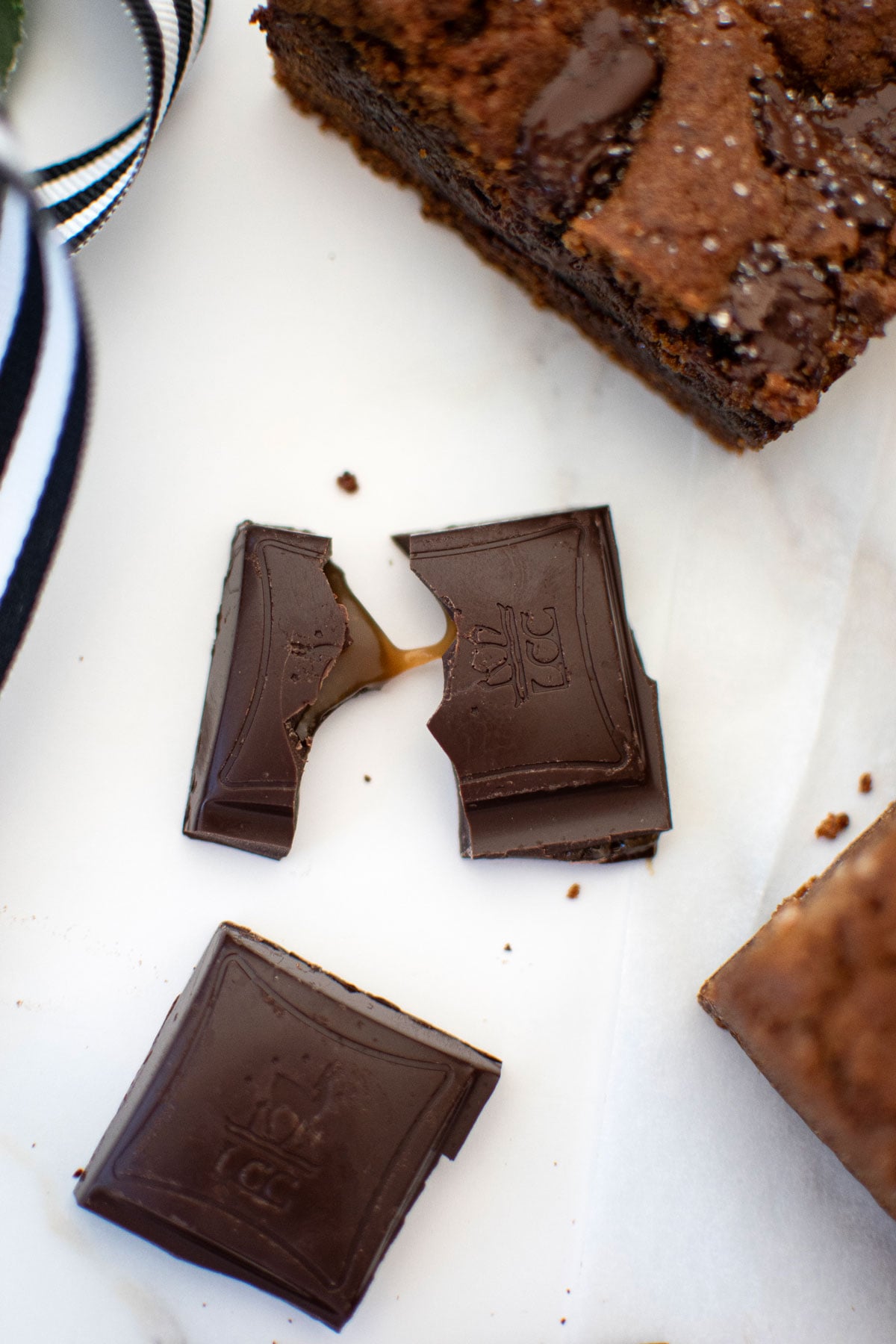 maple caramel dark chocolate square broken in half with caramel coming out on a white marble counter.
