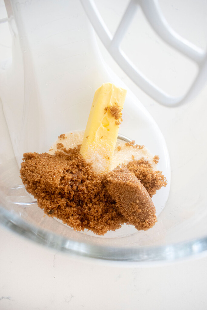 butter and dark brown sugar in a glass mixing bowl on a white marble counter.