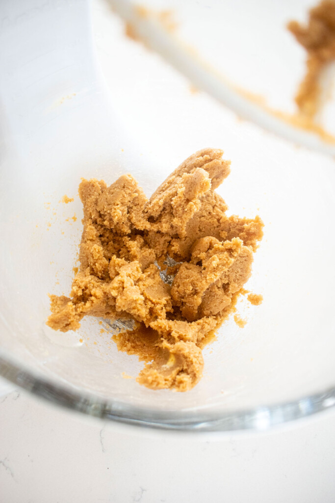 maple caramel dark chocolate gingerbread cookie dough in a glass mixing bowl on a white marble counter.