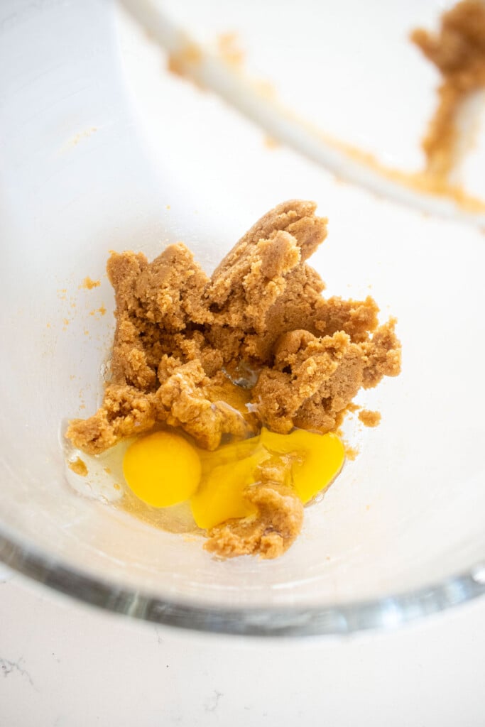 maple caramel dark chocolate gingerbread cookie dough with eggs in a glass mixing bowl on a white marble counter.
